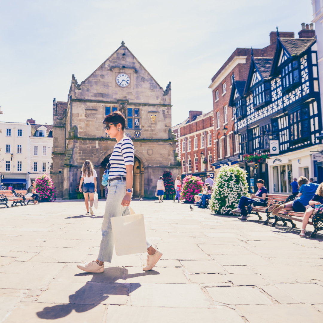 Woman carrying shopping bag through town square, lined with black and white tudor buildings