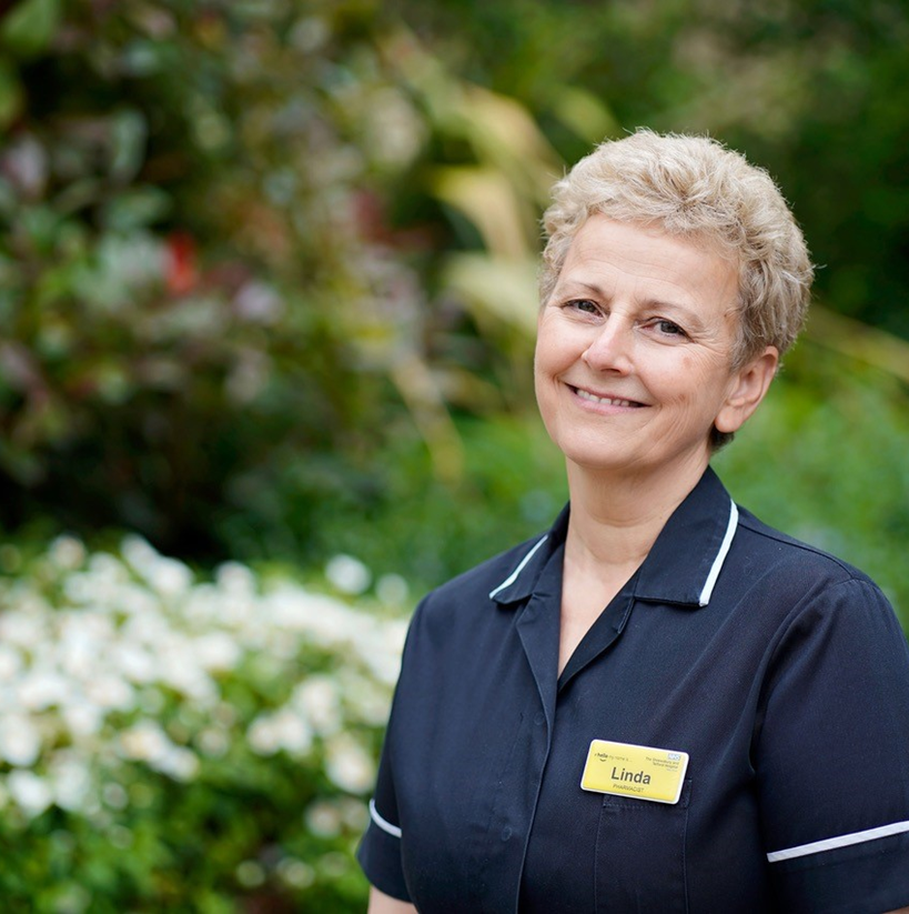 Lady wearing black uniform tunic with a name badge, She is smiling.