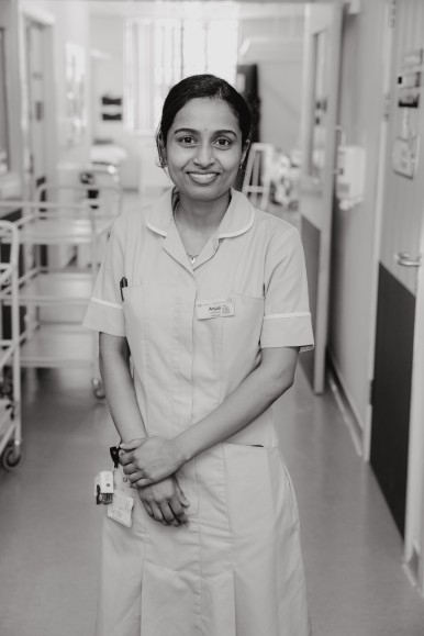 black and white image of nursing standing with hands folded in front, she is smiling