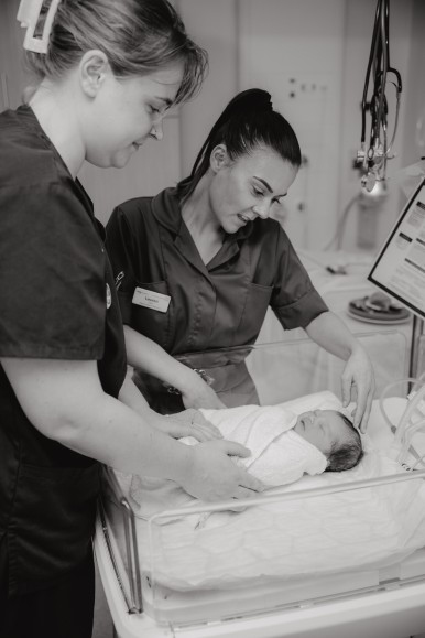 black and white image of nursing staff looking over a baby in a hospital bed