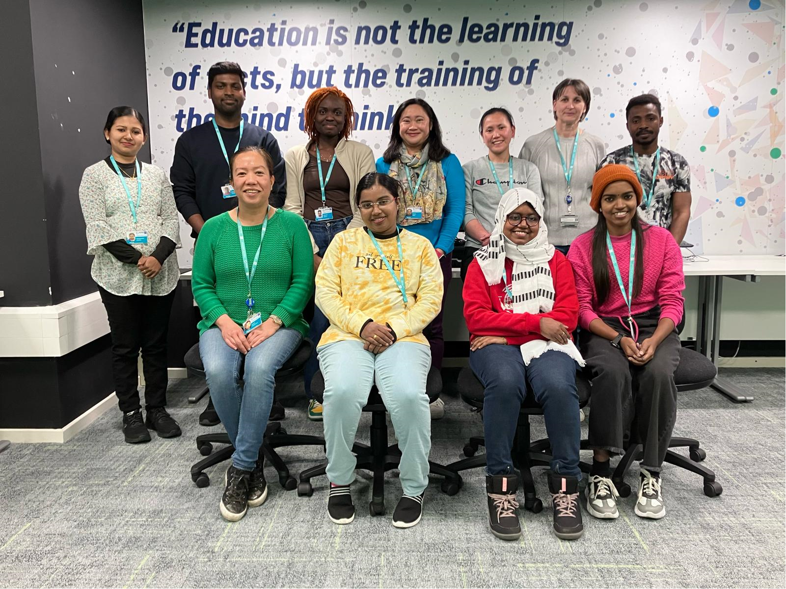 Group of people standing in a room in front of a wall with an Education motto on it.