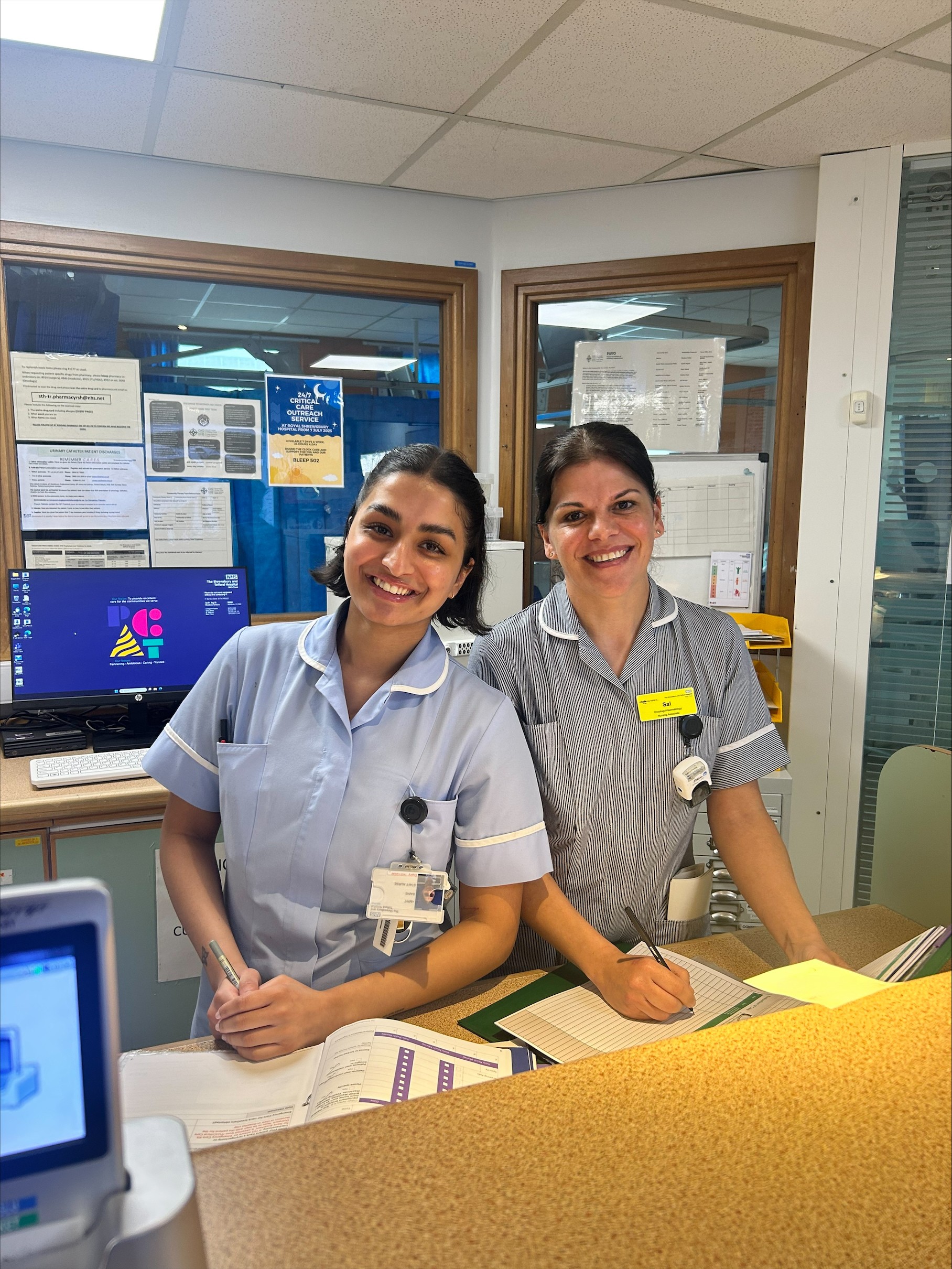 Smiling nursing associate on the ward, next to a registered nurse